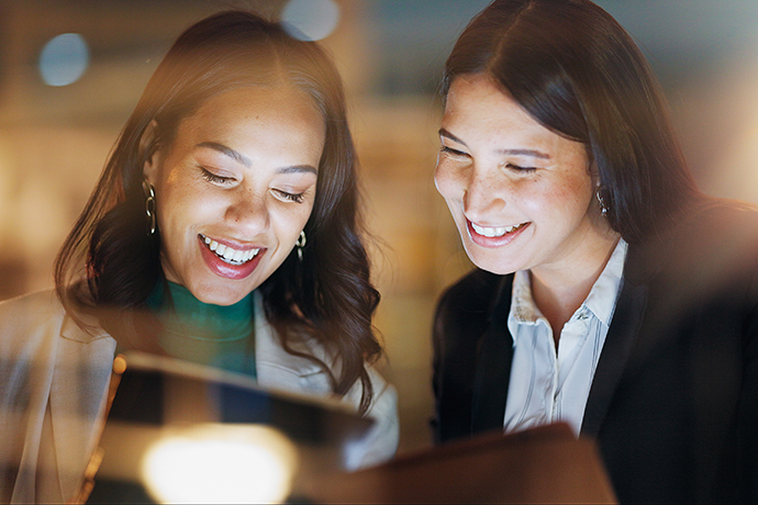 Laptop, tablet and collaboration with business people at night in the office together for teamwork. Technology, smile and a happy employee team of women working on a project or report in the evening