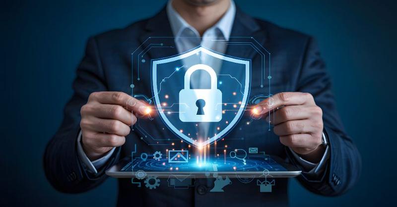 A person in a suit holds a tablet displaying a holographic shield with a padlock, surrounded by digital icons representing cybersecurity. The image conveys secure access and data protection in a modern digital environment.