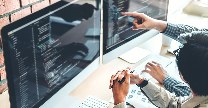 Cyber security professionals reviewing code on computer monitors