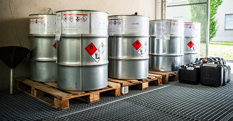 Large metal containers filled with chemical waste from laboratories, featuring colorful barrels arranged in a waste management facility.