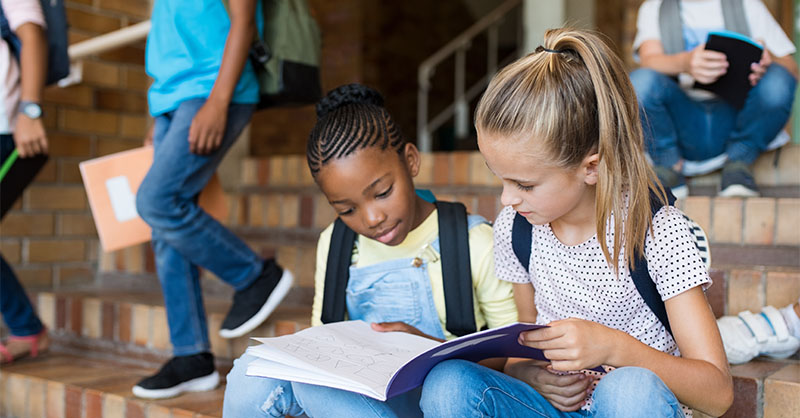 Two young girls on school steps looking at a notebook
